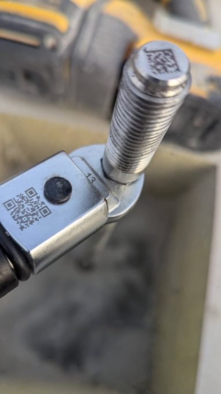 Nahaufnahme eines verchromten Schraubenkopfs mit QR-Code auf einem Werkzeug.
